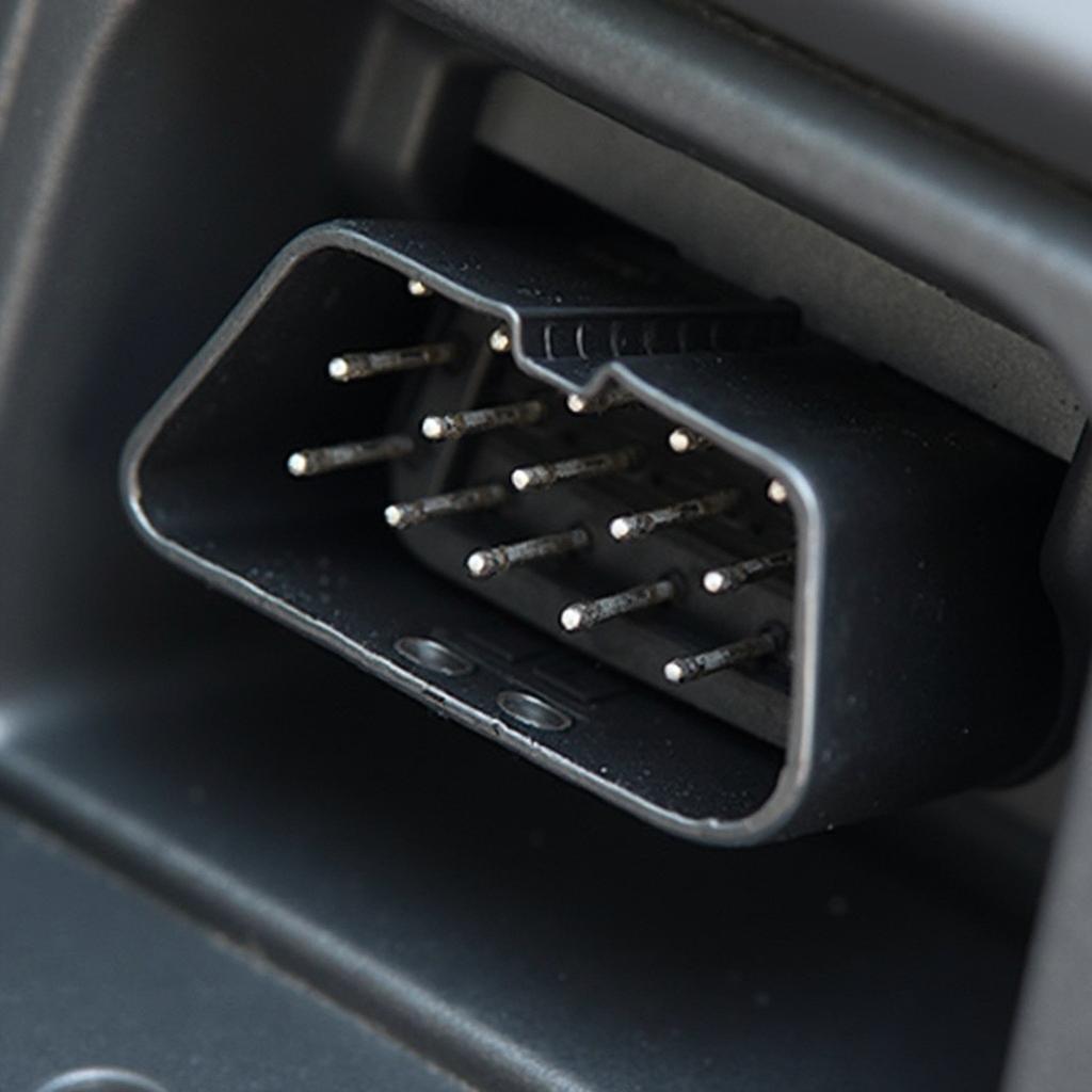 Close-up view of a universal OBD2 16 pin connector plugged into a car's diagnostic port